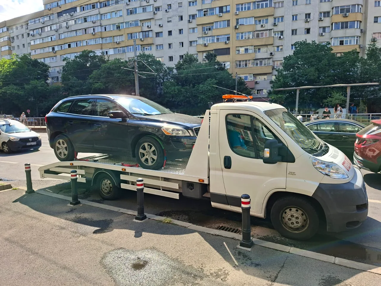 Platforma albă transportă un autoturism negru pe o stradă urbană