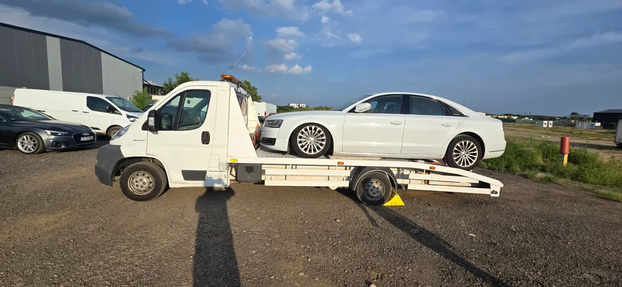 Platforma albă transportând un autoturism pe un drum deschis